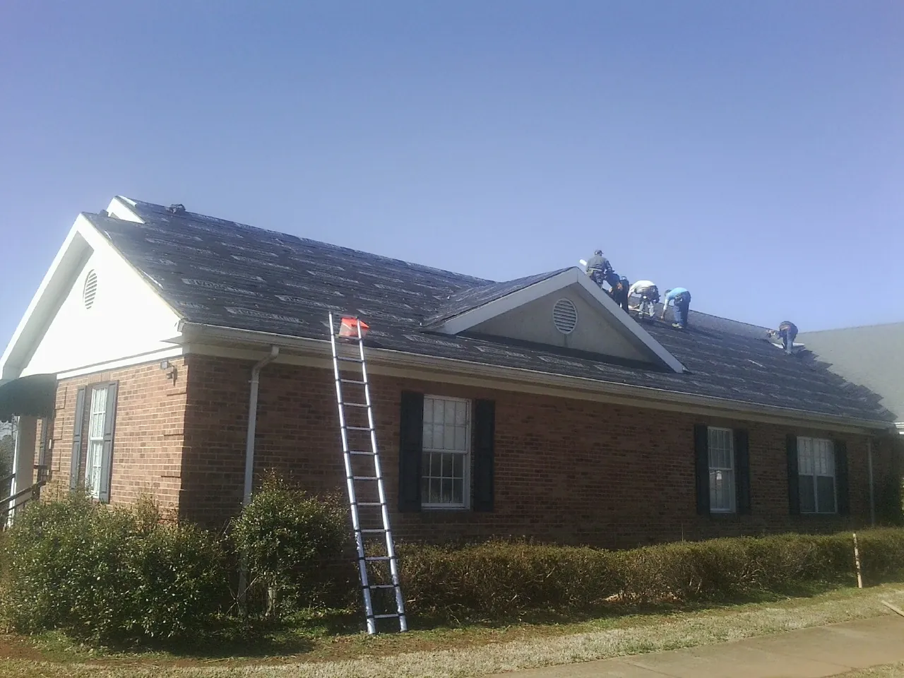 Crew tearing shingles off a brick ranch roof with a ladder set — Emergency Roof Repair work by our crew in Fargo
