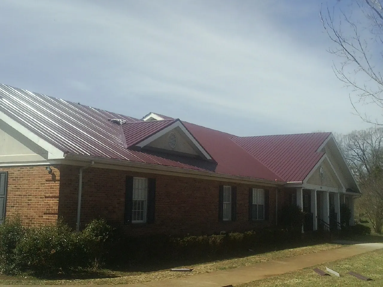 Red metal roof with gabled entries on a long brick building, from a Hail Damage Roof Repair job in Fargo