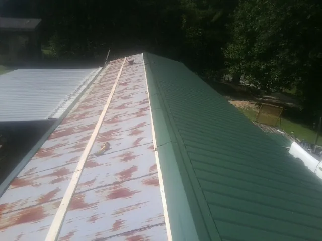 Old rusted panels beside newly installed green metal roofing — Wind Damage Roof Repair by Roofing Brothers in Fargo